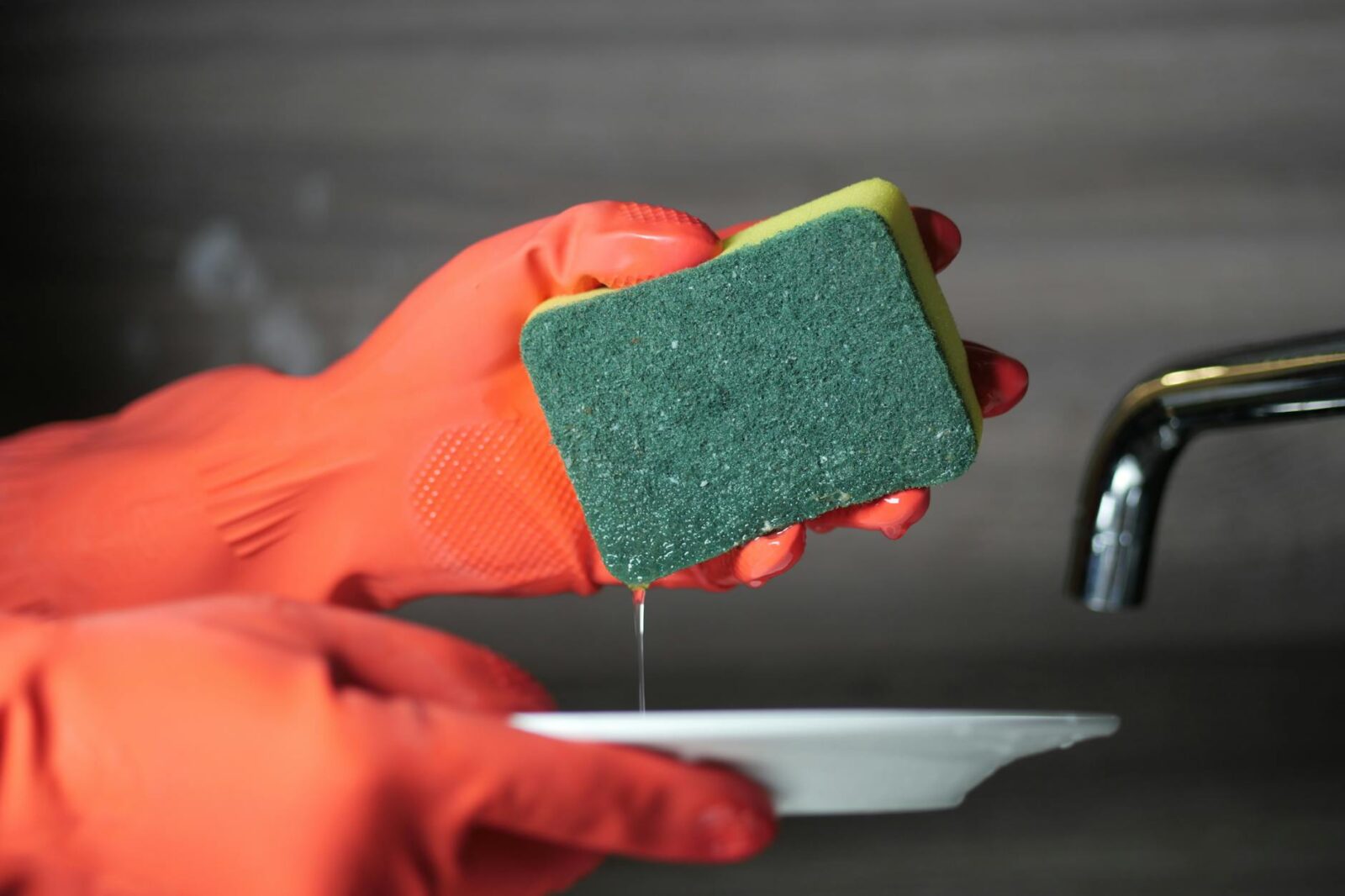 a person wearing rubber gloves while holding a sponge and ceramic plate