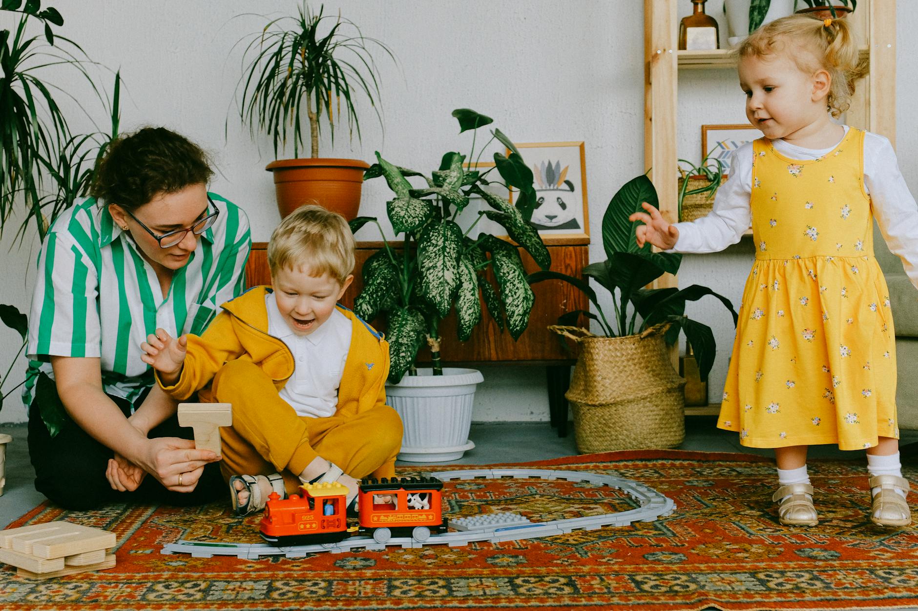 mother and two siblings playing with toy train at home