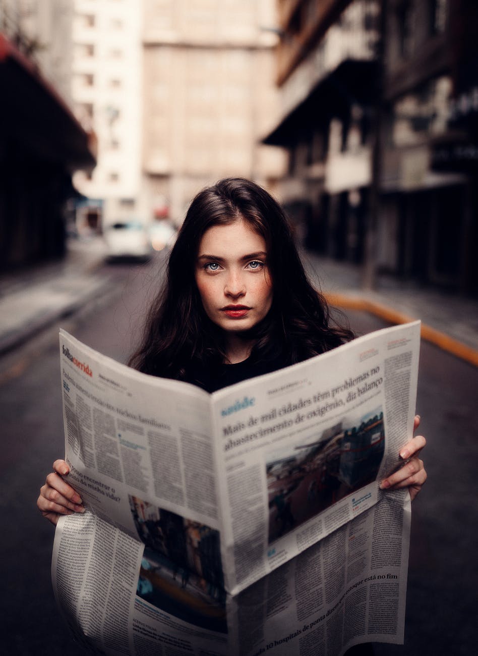 woman in gray sweater holding white newspaper